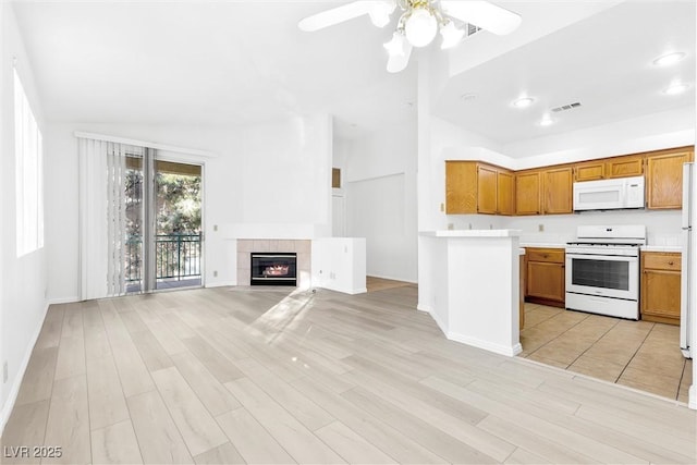 kitchen with a tiled fireplace, white appliances, ceiling fan, and light wood-type flooring