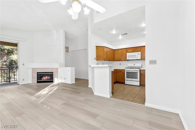 kitchen featuring white appliances, light hardwood / wood-style flooring, a tile fireplace, and ceiling fan