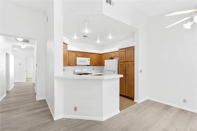 kitchen with white appliances, tile countertops, light wood-type flooring, kitchen peninsula, and ceiling fan