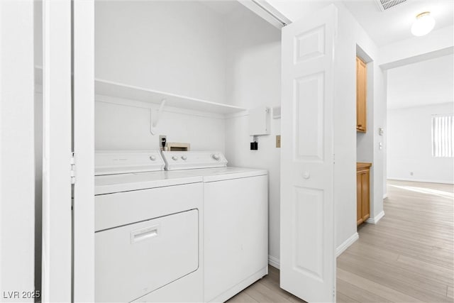 clothes washing area with washing machine and dryer and light hardwood / wood-style flooring