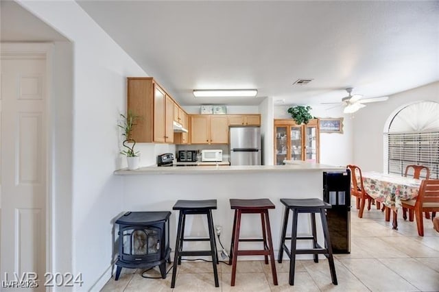 kitchen featuring light brown cabinetry, light tile patterned floors, stainless steel refrigerator, kitchen peninsula, and ceiling fan