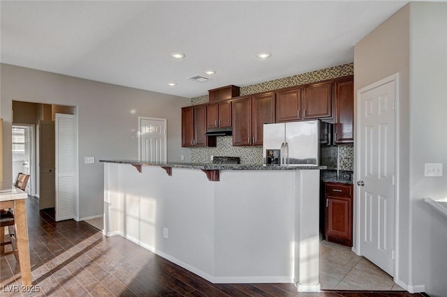 kitchen featuring a breakfast bar, stainless steel fridge with ice dispenser, decorative backsplash, and dark stone countertops