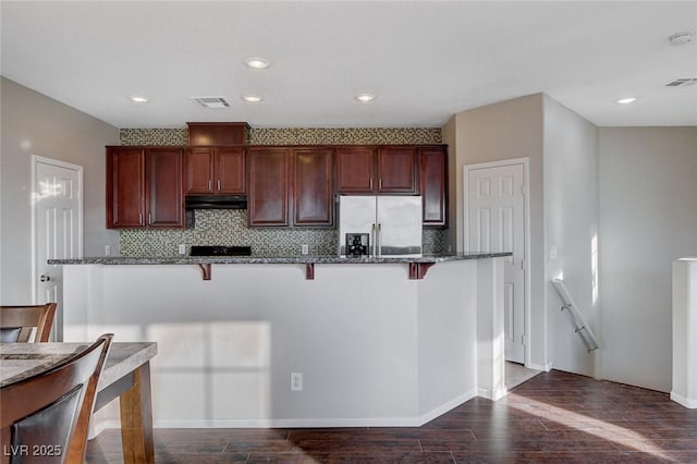 kitchen featuring dark wood-type flooring, a breakfast bar, stainless steel fridge with ice dispenser, and dark stone countertops