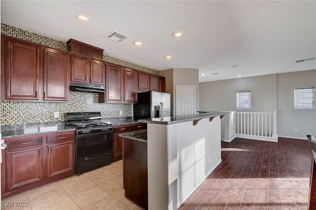 kitchen featuring stainless steel fridge, dark stone countertops, backsplash, a center island, and gas stove