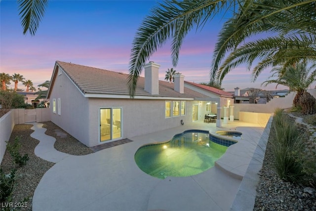 pool at dusk with an in ground hot tub and a patio area