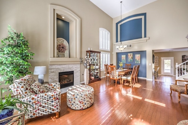 living room with an inviting chandelier, hardwood / wood-style flooring, a fireplace, and high vaulted ceiling