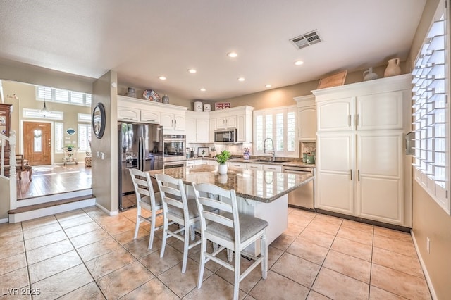 kitchen featuring a breakfast bar area, light tile patterned floors, stainless steel appliances, light stone countertops, and white cabinets