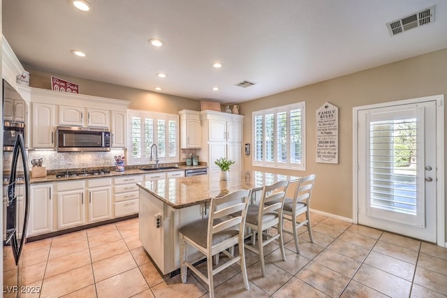 kitchen featuring a breakfast bar area, appliances with stainless steel finishes, a center island, light stone countertops, and white cabinets