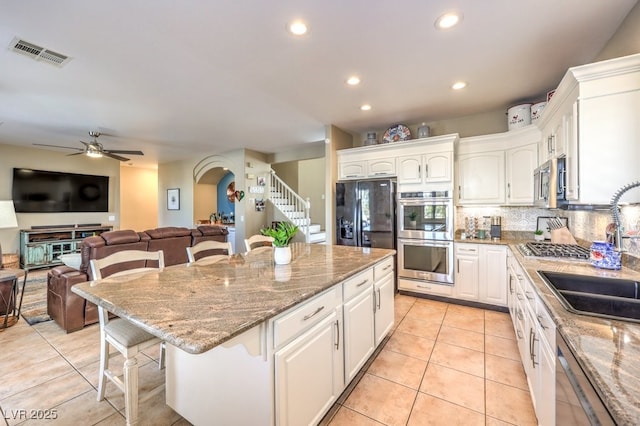 kitchen with white cabinets, a kitchen breakfast bar, a center island, light tile patterned floors, and stainless steel appliances