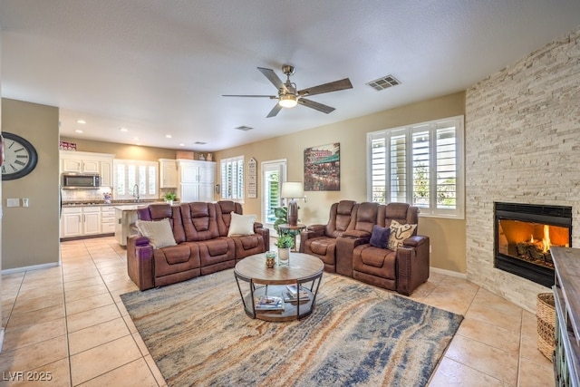 tiled living room featuring ceiling fan, sink, a textured ceiling, and a fireplace