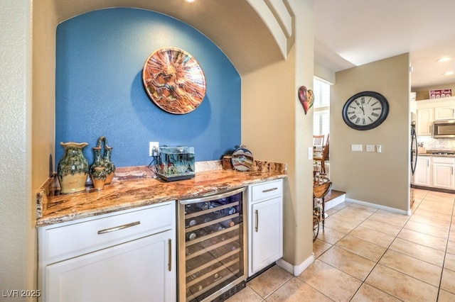 bar featuring white cabinetry, beverage cooler, light stone counters, and light tile patterned floors