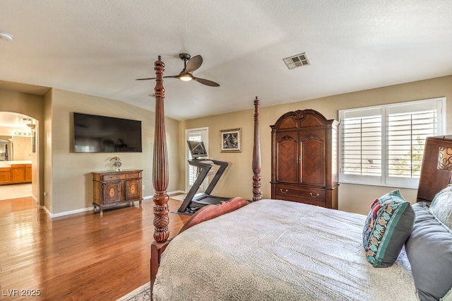 bedroom with connected bathroom, wood-type flooring, vaulted ceiling, a textured ceiling, and ceiling fan