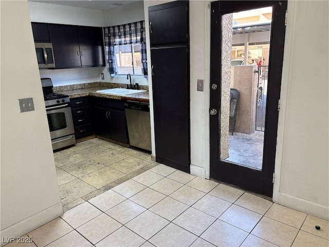 kitchen with dark cabinetry, baseboards, light tile patterned flooring, a sink, and appliances with stainless steel finishes