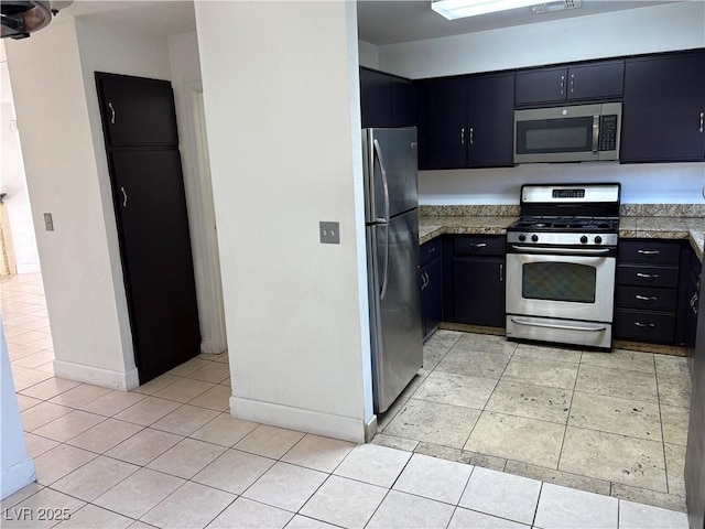 kitchen with light tile patterned floors, stainless steel appliances, dark cabinetry, and baseboards