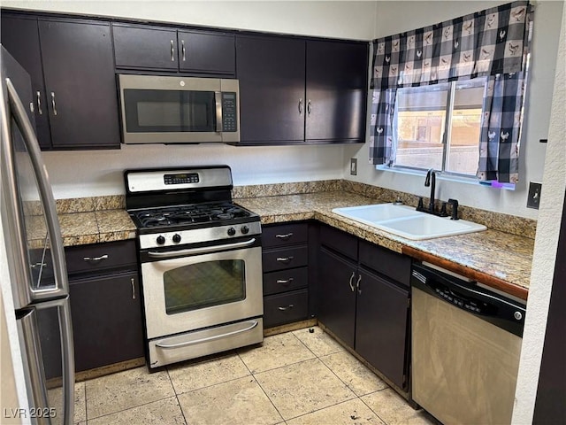 kitchen featuring a sink, dark cabinetry, tile countertops, appliances with stainless steel finishes, and light tile patterned floors