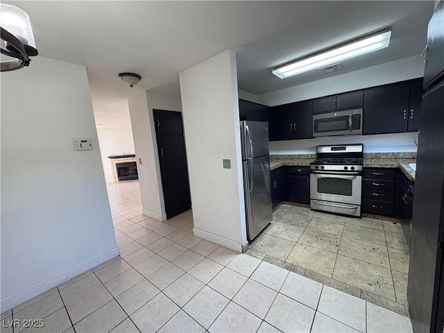 kitchen featuring visible vents, a tiled fireplace, light tile patterned floors, appliances with stainless steel finishes, and dark cabinets