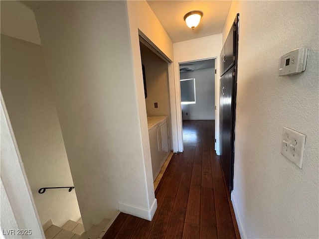 hall featuring dark wood finished floors, a textured wall, and baseboards