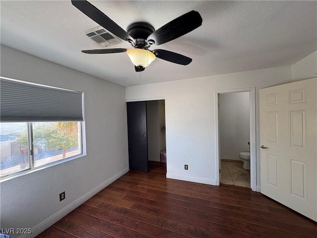 unfurnished bedroom with visible vents, a textured ceiling, hardwood / wood-style floors, connected bathroom, and baseboards