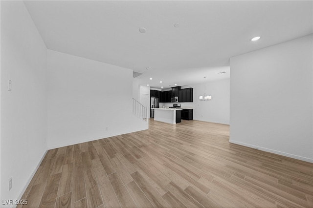 unfurnished living room with an inviting chandelier and light hardwood / wood-style flooring