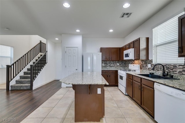 kitchen featuring light stone counters, sink, white appliances, and a center island