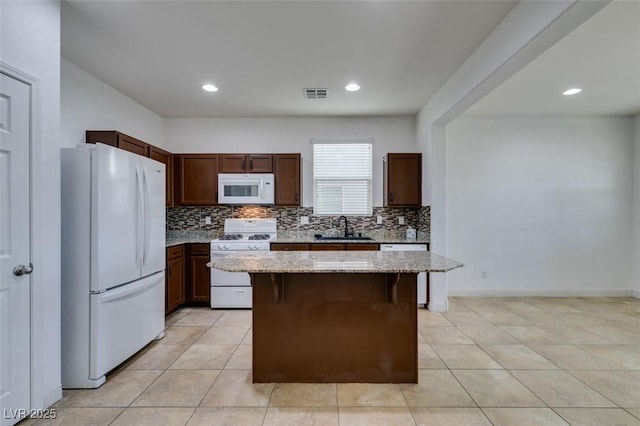 kitchen featuring sink, a breakfast bar area, light stone counters, a center island, and white appliances