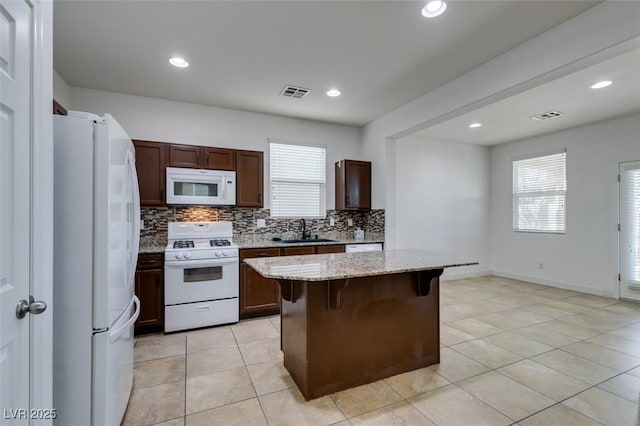 kitchen with sink, a breakfast bar area, light stone counters, a kitchen island, and white appliances