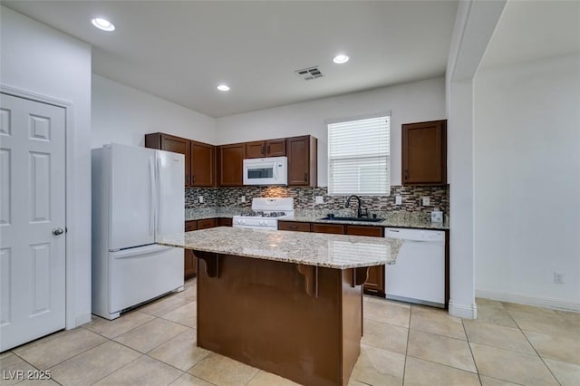 kitchen with light tile patterned flooring, sink, a center island, a kitchen breakfast bar, and white appliances