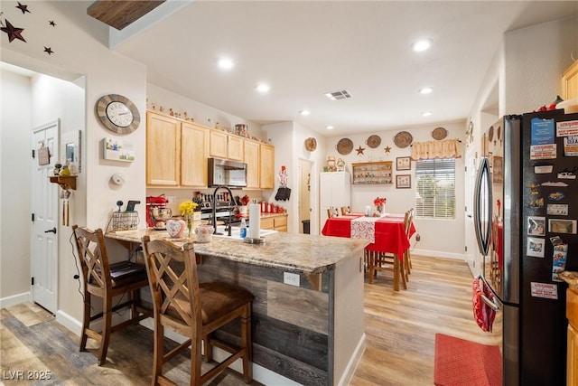 kitchen featuring light hardwood / wood-style flooring, a breakfast bar, appliances with stainless steel finishes, light stone counters, and light brown cabinetry