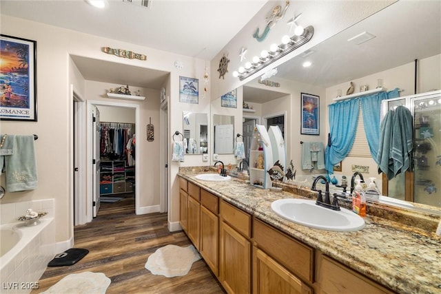 bathroom with hardwood / wood-style flooring, vanity, and tiled tub