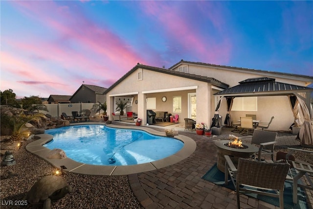 pool at dusk featuring a gazebo, a patio area, and an outdoor fire pit