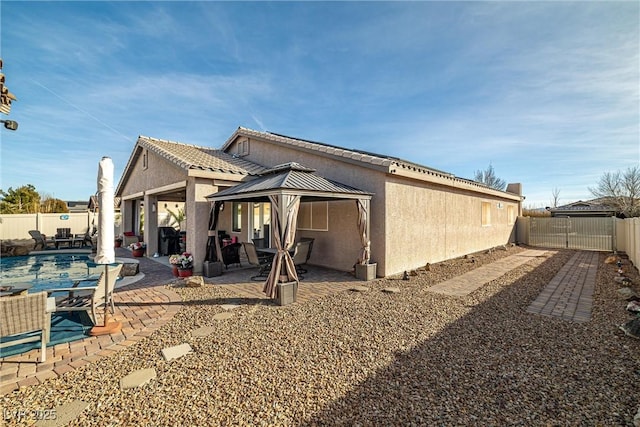 rear view of house with a fenced in pool, a gazebo, and a patio area