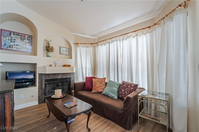 living room featuring a tiled fireplace, a healthy amount of sunlight, and dark hardwood / wood-style flooring