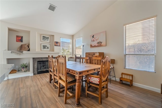 dining area with lofted ceiling, wood-type flooring, and a tiled fireplace