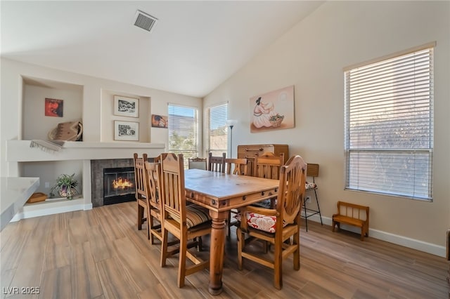 dining area with hardwood / wood-style flooring, a tiled fireplace, and vaulted ceiling