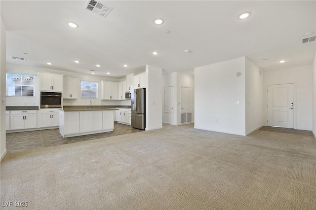 kitchen with light colored carpet, a center island, white cabinets, and appliances with stainless steel finishes