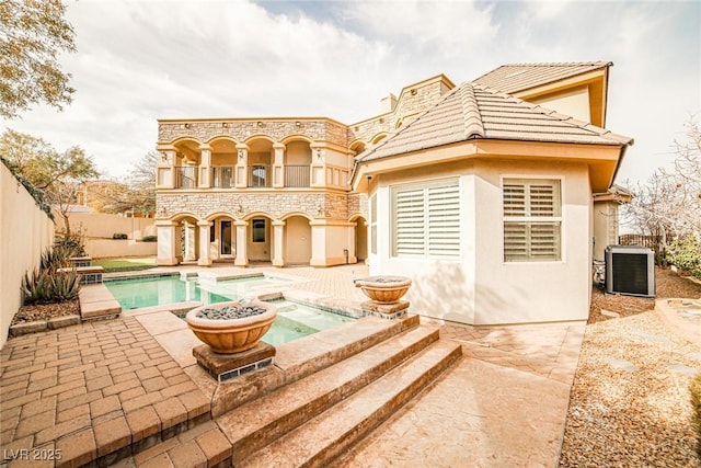 rear view of property with central AC, a balcony, a pool with hot tub, and a patio area