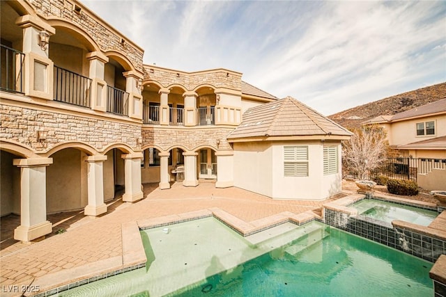 rear view of property with a balcony, a pool with hot tub, and a patio area