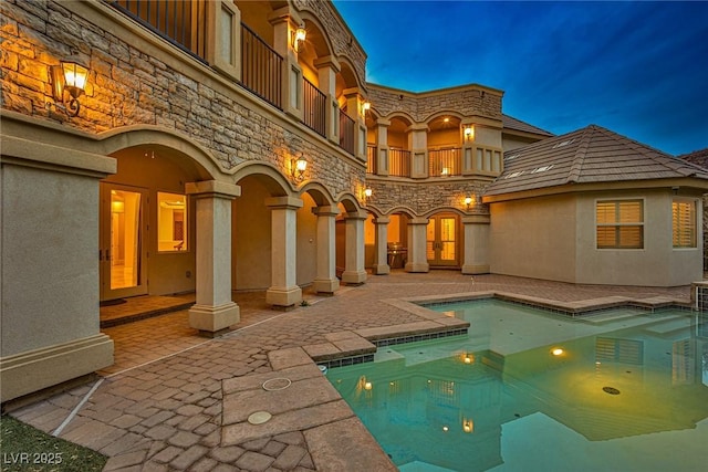 back house at dusk featuring a balcony and a patio area