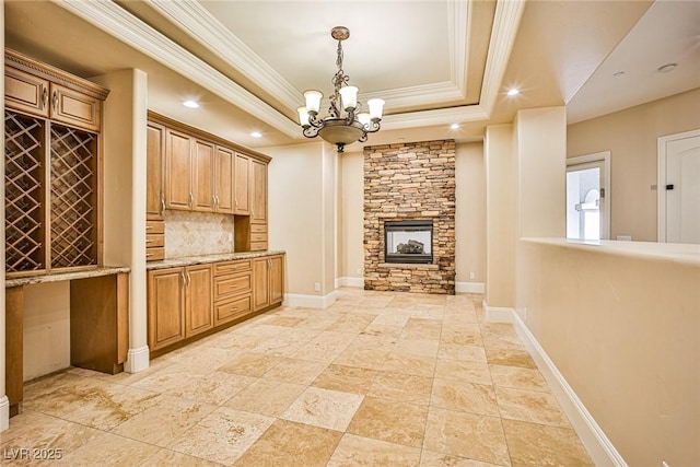 interior space with a stone fireplace, ornamental molding, a raised ceiling, and a chandelier