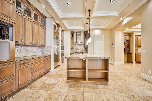 kitchen with light stone countertops, wall chimney range hood, built in appliances, and decorative light fixtures