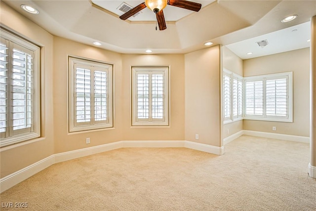 empty room featuring ceiling fan, light colored carpet, a healthy amount of sunlight, and a raised ceiling