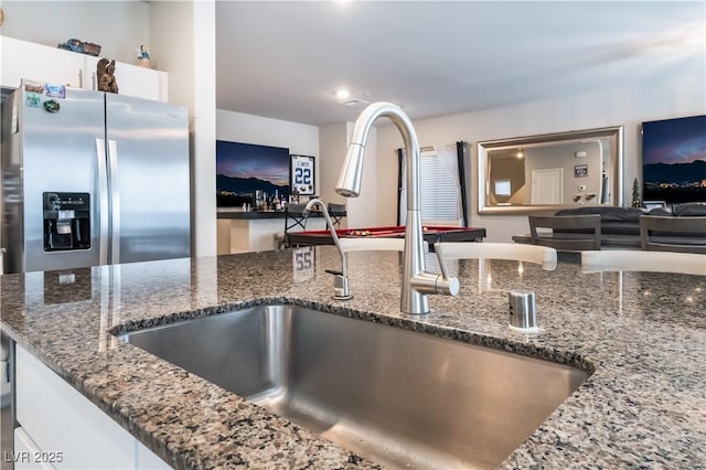 kitchen with dark stone counters, stainless steel fridge with ice dispenser, sink, and white cabinets