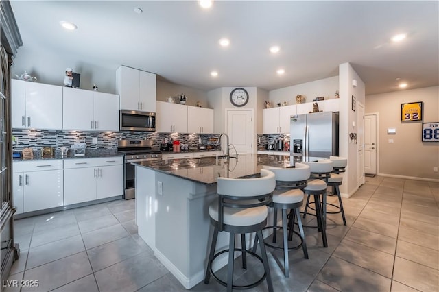 kitchen featuring a breakfast bar, white cabinets, decorative backsplash, stainless steel appliances, and a center island with sink