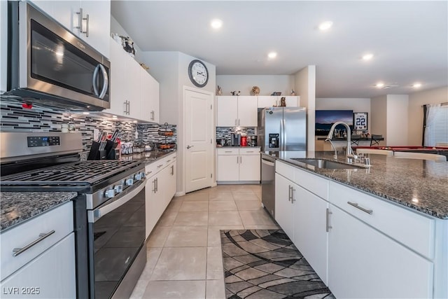 kitchen featuring sink, light tile patterned floors, appliances with stainless steel finishes, white cabinetry, and dark stone counters