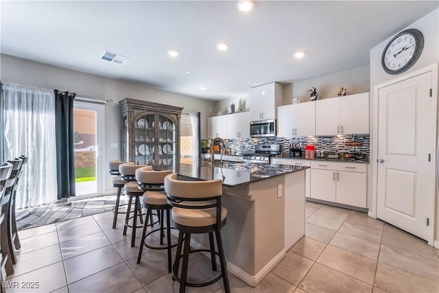 kitchen featuring light tile patterned floors, stainless steel appliances, an island with sink, and white cabinets