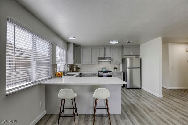 kitchen with a breakfast bar area, gray cabinets, kitchen peninsula, stainless steel appliances, and decorative backsplash