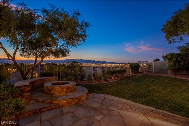 patio terrace at dusk with a mountain view, a fire pit, and a lawn