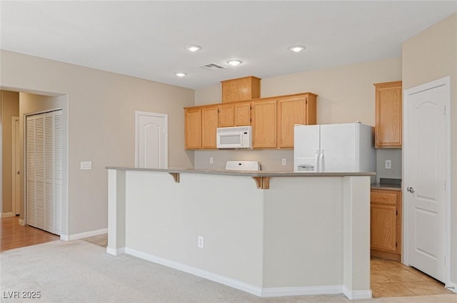 kitchen featuring a kitchen bar, a center island, light carpet, light brown cabinets, and white appliances