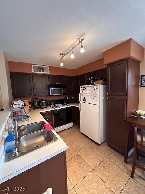 kitchen with light tile patterned flooring, white appliances, dark brown cabinetry, and sink