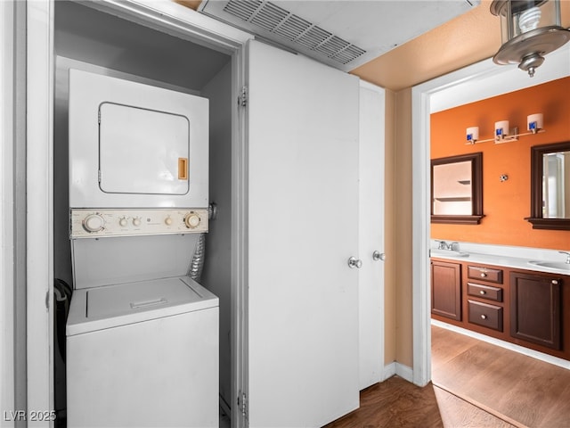 laundry room with dark wood-style floors, stacked washer and dryer, a sink, laundry area, and baseboards